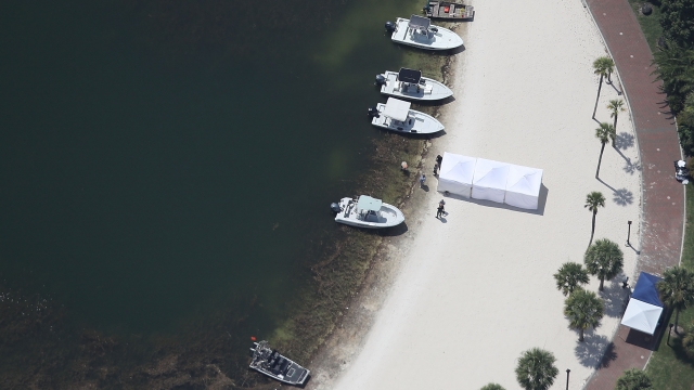A view from above of white search boats on the shore while a white tent sits on the beach.