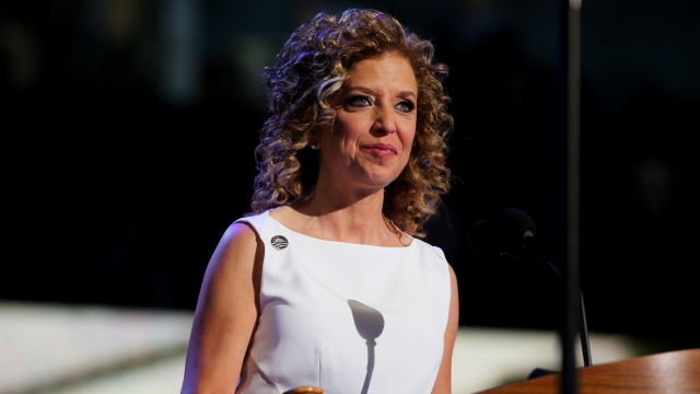 Debbie Wasserman Schultz wearing a white sleeveless dress stands at the podium at the Democratic National Convention.