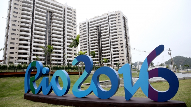 A Rio 2016 sign is in the foreground of the Olympic Village with two high-rise buildings in the background