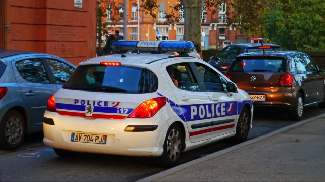A white French police car with red and blue stripes is parked on a street.