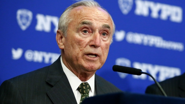 NYPD Commissioner William Bratton stands at a podium with a microphone.