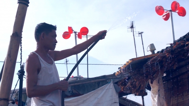 A Vietnamese man sprays a hose in a slum with red plastic bucket wind turbines