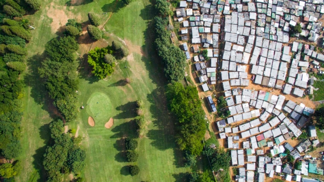 A tree-lined fence separates the lush, green Papwa Sewgolum Golf Course from a settlement of tin shacks in South Africa.
