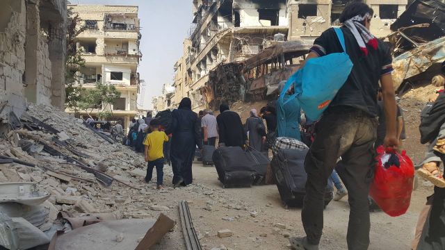Citizens of Daraya evacuate, walking past the rubble of the badly damaged city.