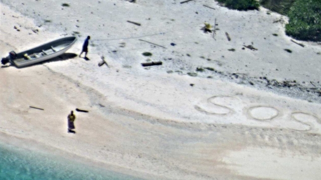 Two people stranded on an island where they wrote "SOS" in the sand