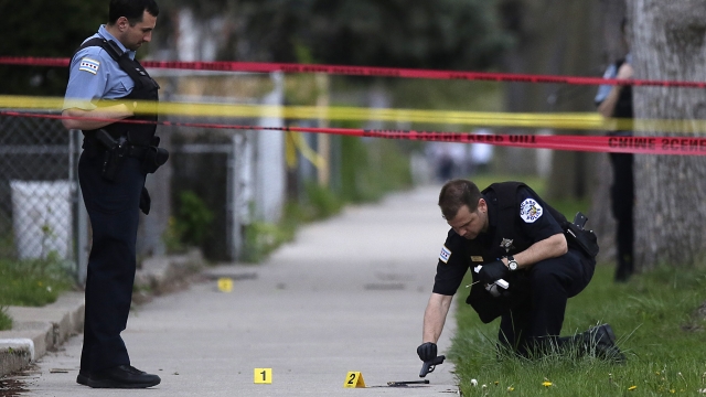 A Chicago Police officer, left, watches as an evidence technician officer investigates a gun at a murder scene.