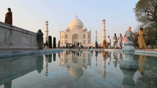 The Taj Mahal stands in the distance as its image is reflected in a pool.