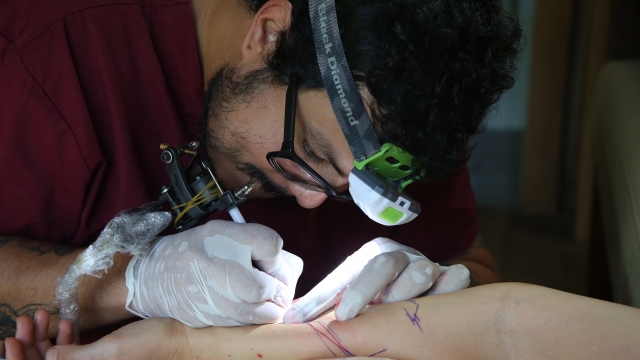 Juan Carlos Mendoza uses hues of red and violet as he tattoos someone's arm.