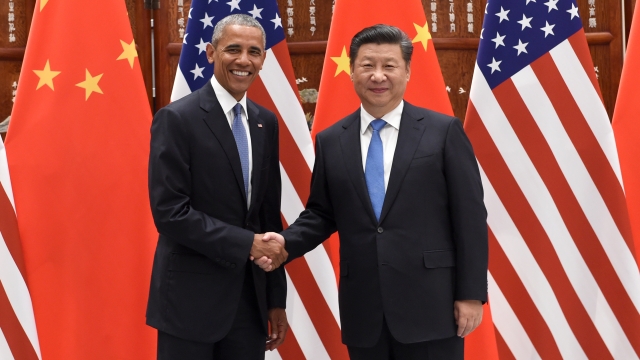 Barack Obama and Xi Jinping shaking hands in front of US and Chinese flags.