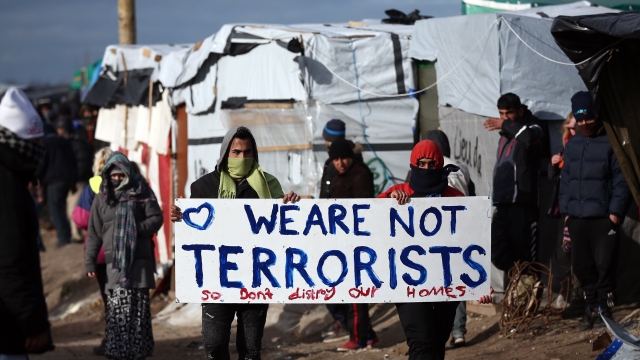 Two people hold a sign that says "We are not terrorists so don't destroy our homes" at the migrant camp in Calais, France