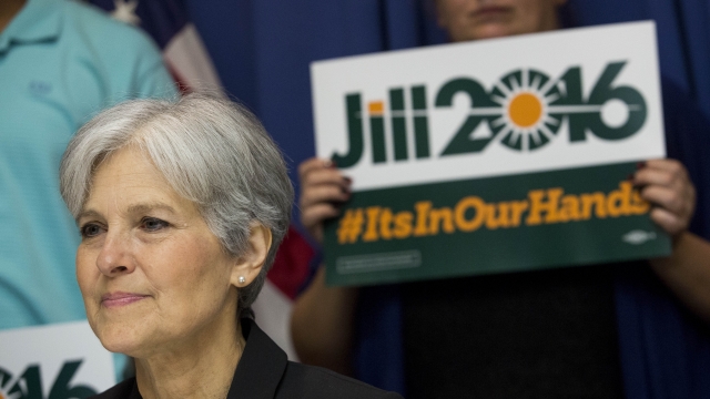 Jill Stein. A person behind her holds a Jill Stein 2016 banner.