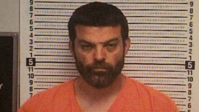 Toby Willis, with a full head of brown hair and brown beard and mustache, wears an orange prison suit and stares straight.