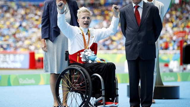 Marieke Vervoort wears a white and red jacket. She has bleach blonde short hair. She sits in her wheelchair with arms raised.