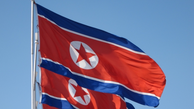 North Korean flags fly. They have a blue and white top and bottom. The middle is red with a white circle and red star.