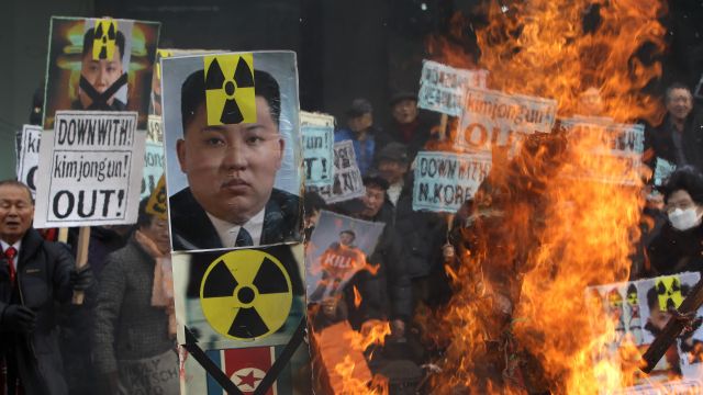Fire burns alongside people holding signs with Kim Jong-un and nuclear symbols at an anti-Kim Jong-un protest in Seoul