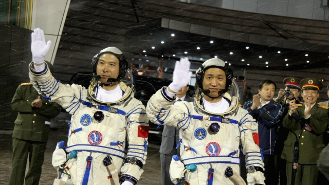 Chinese astronauts wave before boarding their spacecraft.