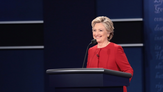 Hillary Clinton stands at a podium with a microphone and smiles.