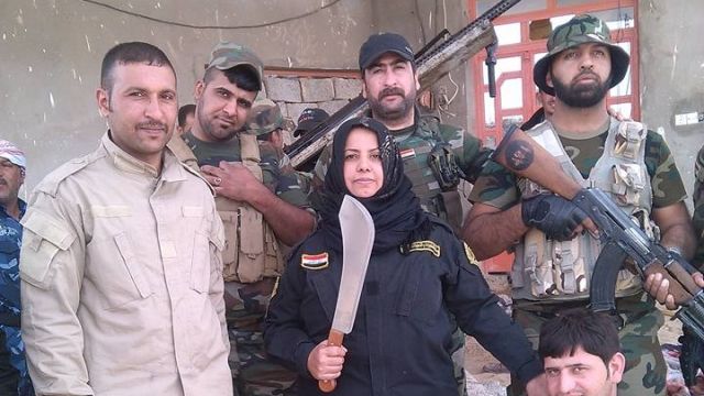 Um Hanadi holds up a machete with Iraqi soldiers around her. She claims to have beheaded ISIS fighters.