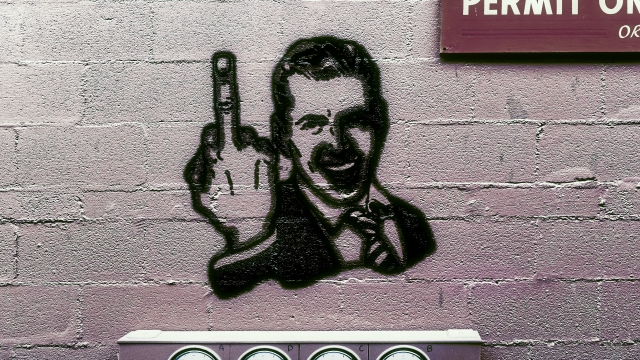 A spray-painted figure flashes a middle finger on a brick wall.