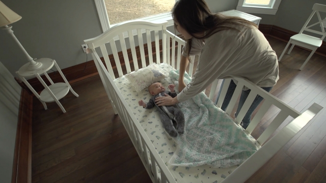 A woman puts a baby in a crib