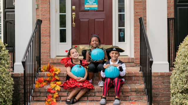 Kids dressed in Halloween costumes hold teal pumpkins.
