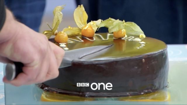 A hand holding a knife cuts a cake in a still from the BBC's final season of the "The Great British Bake Off."