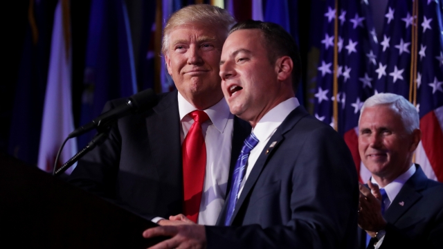 Reince Priebus speaks while Donald Trump and Mike Pence stand behind him.