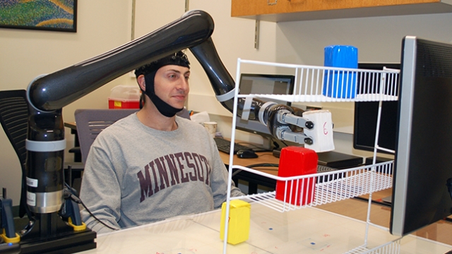 A man wearing an EEG cap controls a robotic arm.