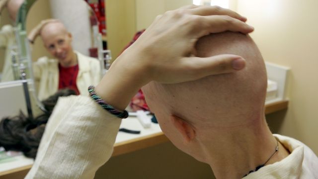 A breast cancer patient rubs her head before trying on a wig.