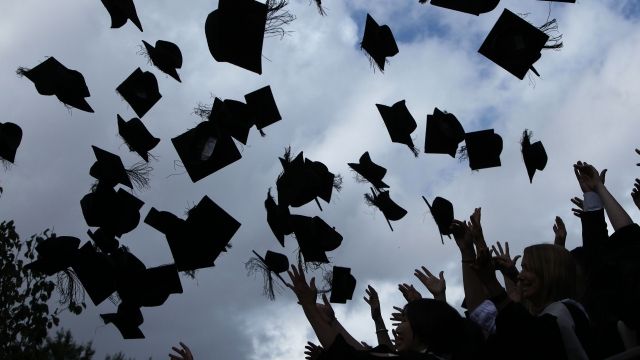 Students throw their mortarboards in the air during their graduation.