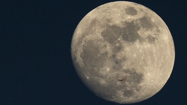 An plane flies in front of the moon
