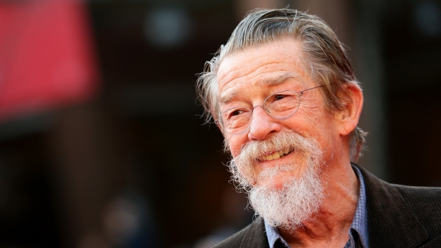 John Hurt appears on a red carpet.
