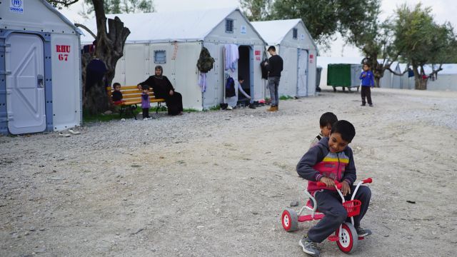 Refugee children play in front of a camp shelter