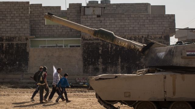 Civilians hold a white flag as they pass an Iraqi Army Armoured Ninth Division tank