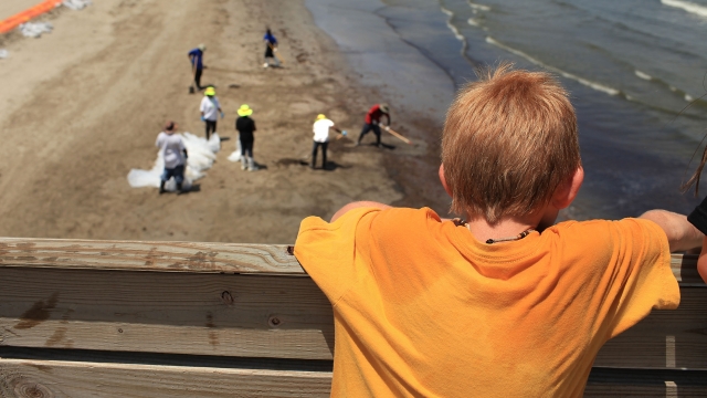 A boy watches workers clean oil off a beach after an oil spill