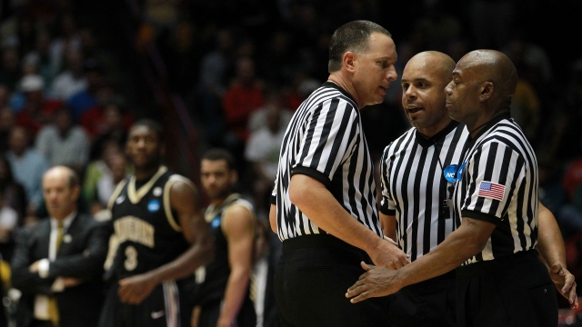 NCAA basketball referees discuss a call during a game