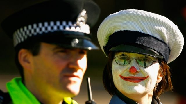 A clown stands next to a police officer.