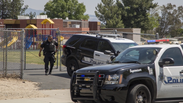 A police officer stands outside the fence leading to the school.
