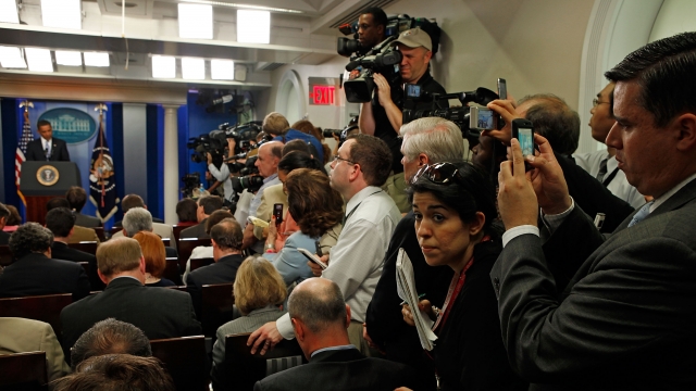 Reporters squeeze in the aisle while using hand-held digital devices.