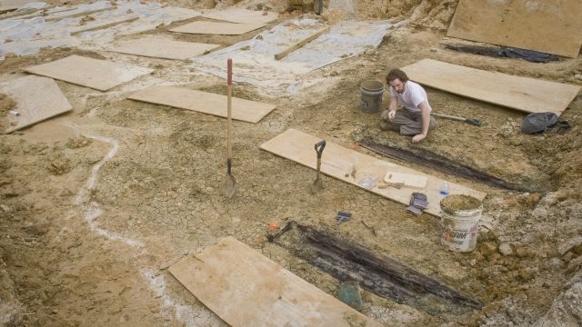 Forrest Follet from Mississippi State University removes the soil from the lid of a grave uncovered during construction.