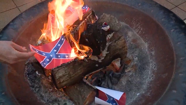 A person puts a confederate flag in a fire pit