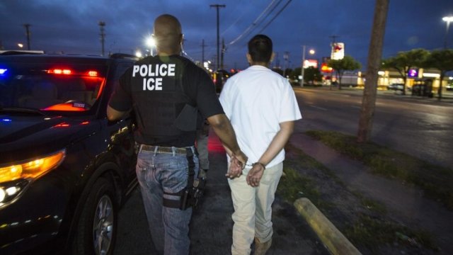 An Immigration and Customs Enforcement officer handcuffs a man.