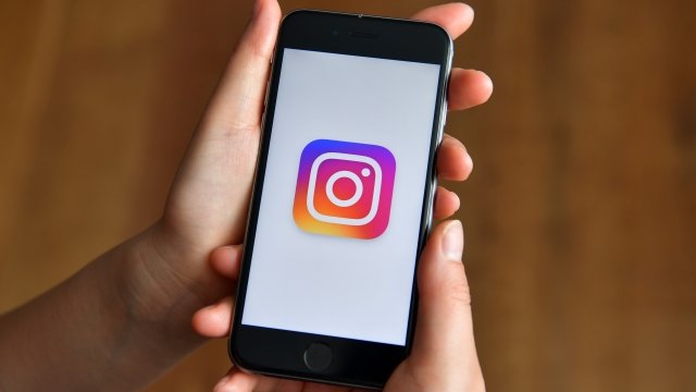 Person holds a phone displaying the Instagram logo