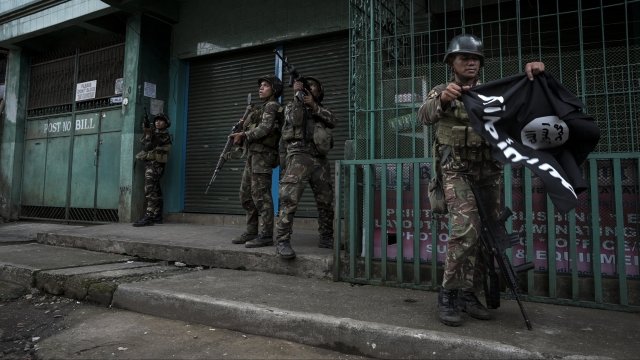 A soldier in Marawi, Philippines, carries a captured ISIS flag while clearing a city street of militants.