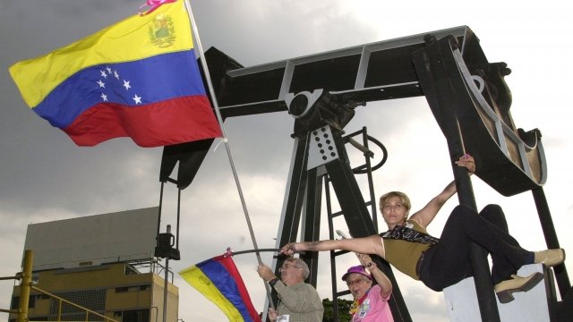 Venezuelan protesters wave flags in front of an oil drilling monument.