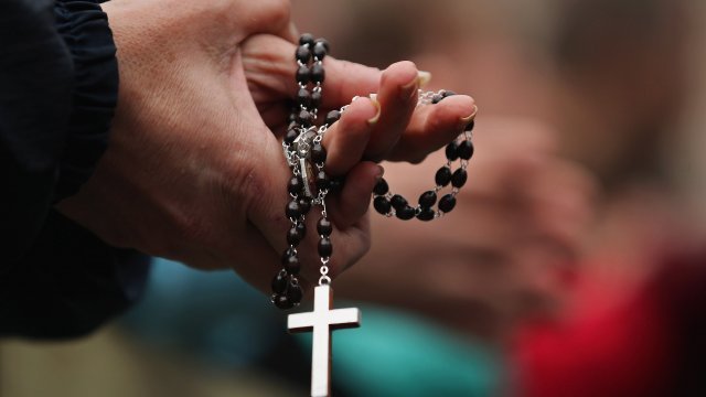 A priest holds a rosary with a cross.