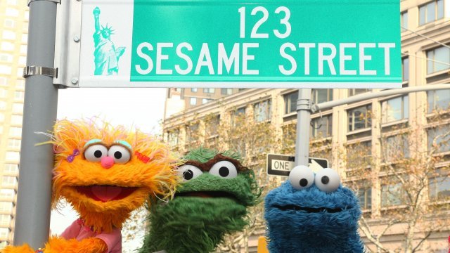 Characters of "Sesame Street" stand by street sign.