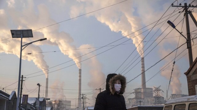 Smoke billows from stacks as a Chinese woman wears as mask.