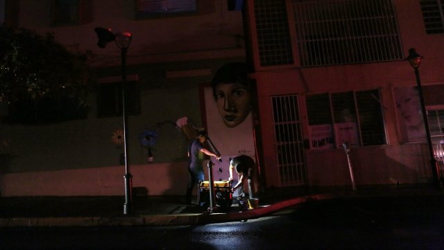 A man prepares to fill a generator with gas to power a bar on a darkened street.