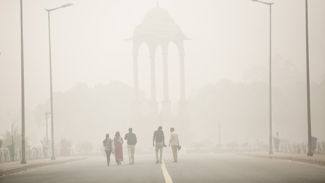 People walk near India gate amid heavy dust and smog